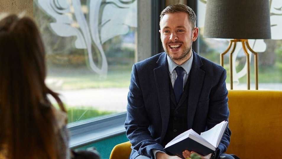 man in dark blue suit sitting on chair smiling